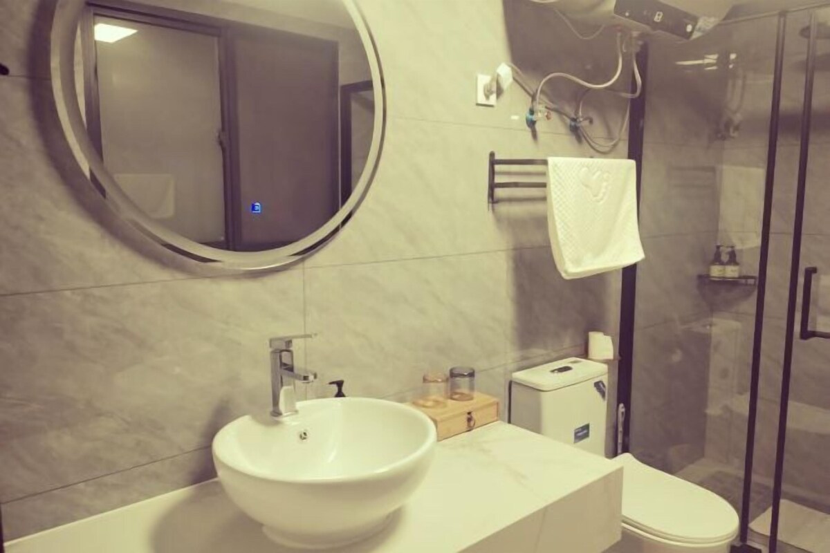 Une salle de bain avec un miroir rond, un lavabo, des toilettes et une douche à parois de verre.