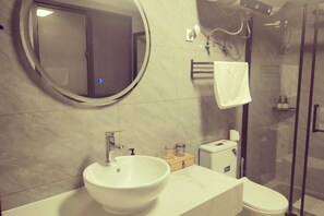 Une salle de bain avec un miroir rond, un lavabo, des toilettes et une douche à parois de verre.