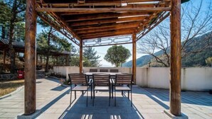 A covered outdoor seating area with a table and chairs, surrounded by stone steps and a view of trees and mountains.