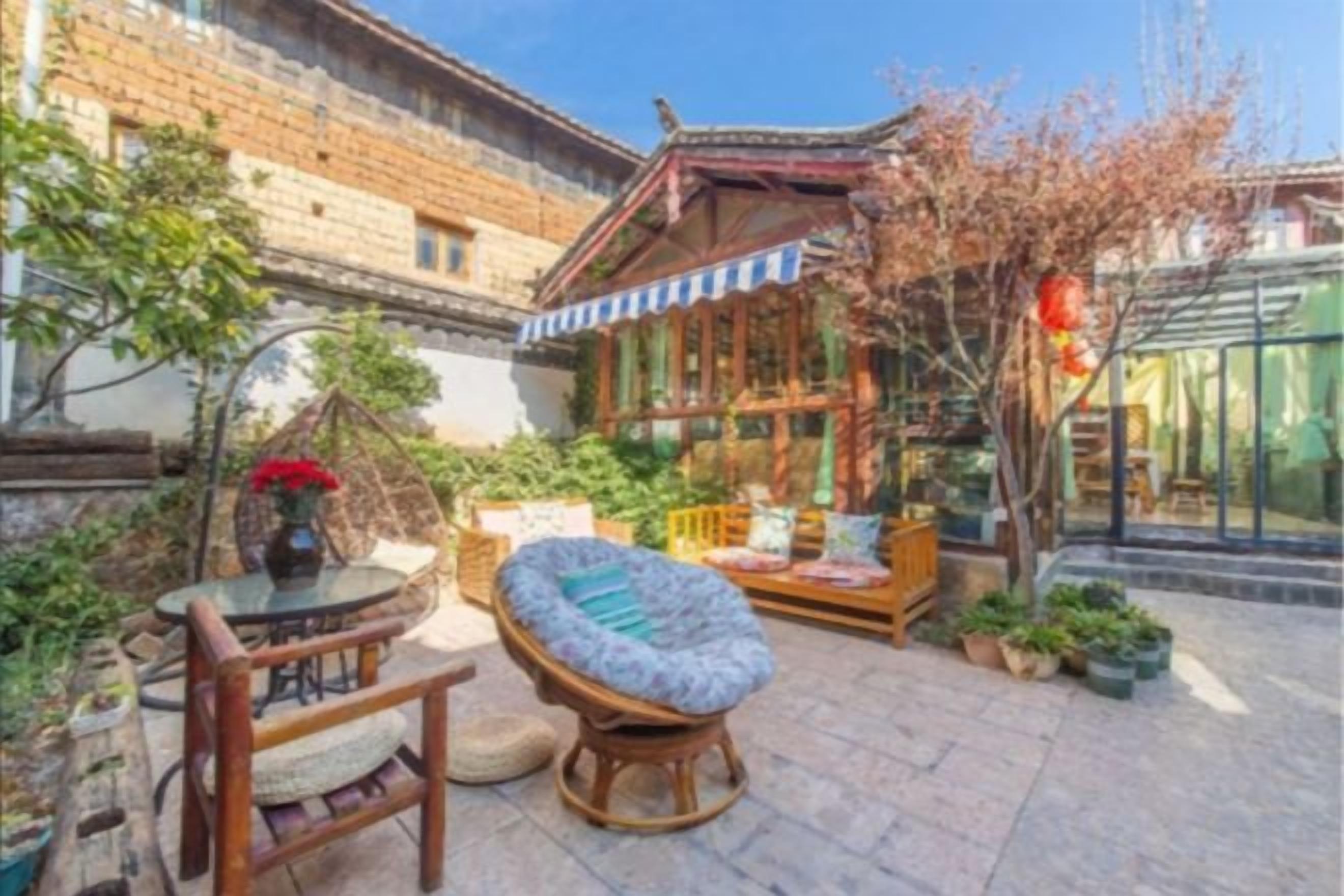 A courtyard with traditional architecture, including a wooden structure with a tiled roof, a seating area with cushions, and a table with chairs.
