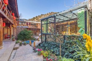 A traditional courtyard with a glass greenhouse, wooden structures, and potted plants. - Flowers Hotel (Lijiang)