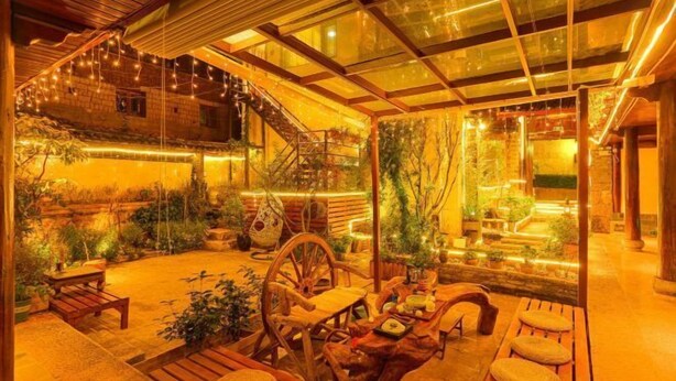 Une terrasse extérieure accueillante, avec des meubles en bois, une cheminée en pierre et des guirlandes lumineuses.
