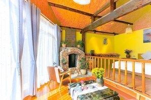 Un salon chaleureux avec une cheminée en pierre, des poutres en bois et un mur jaune.