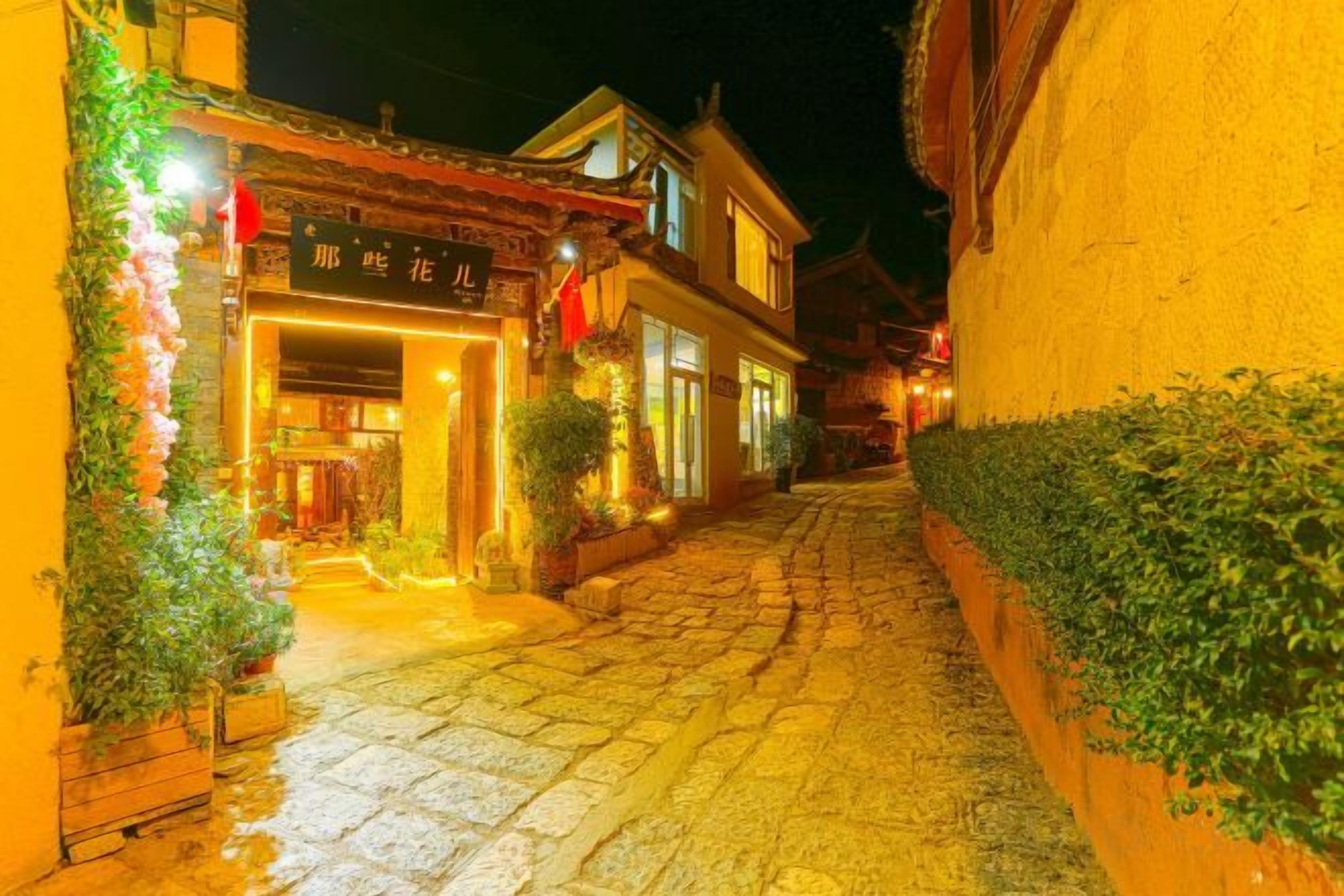 Una calle estrecha flanqueada por edificios, una tienda con un letrero y una entrada bien iluminada.