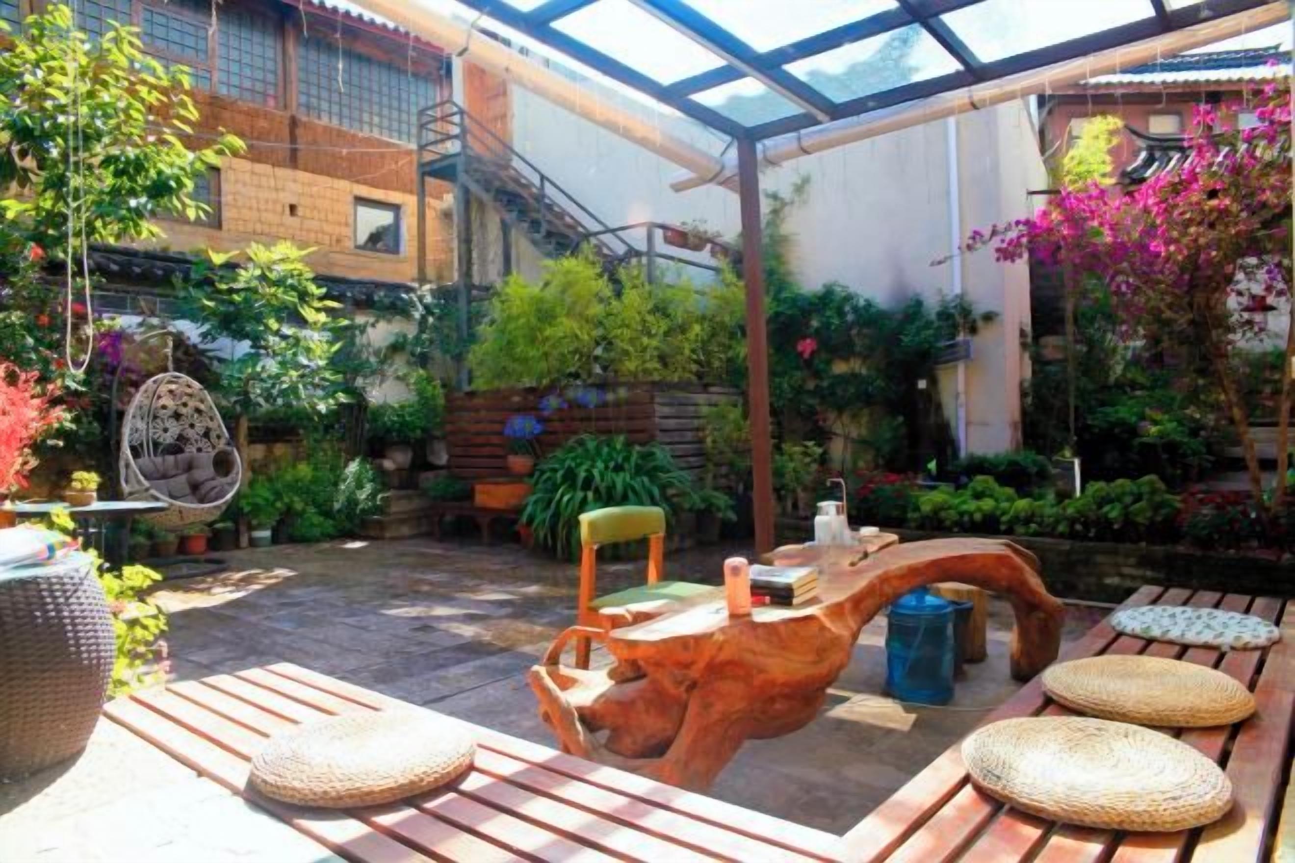 Un porche cubierto con mobiliario de madera, un sillón colgante y plantas en macetas.