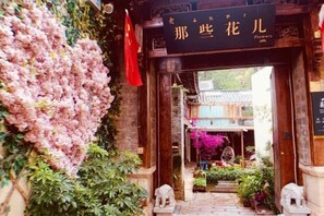 A traditional Chinese gate with a sign, surrounded by lush greenery and flowers. - Flowers Hotel (Lijiang)