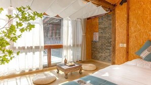 Une pièce avec un lit, une petite table, une fenêtre avec des rideaux, un mur en bois et une plante.