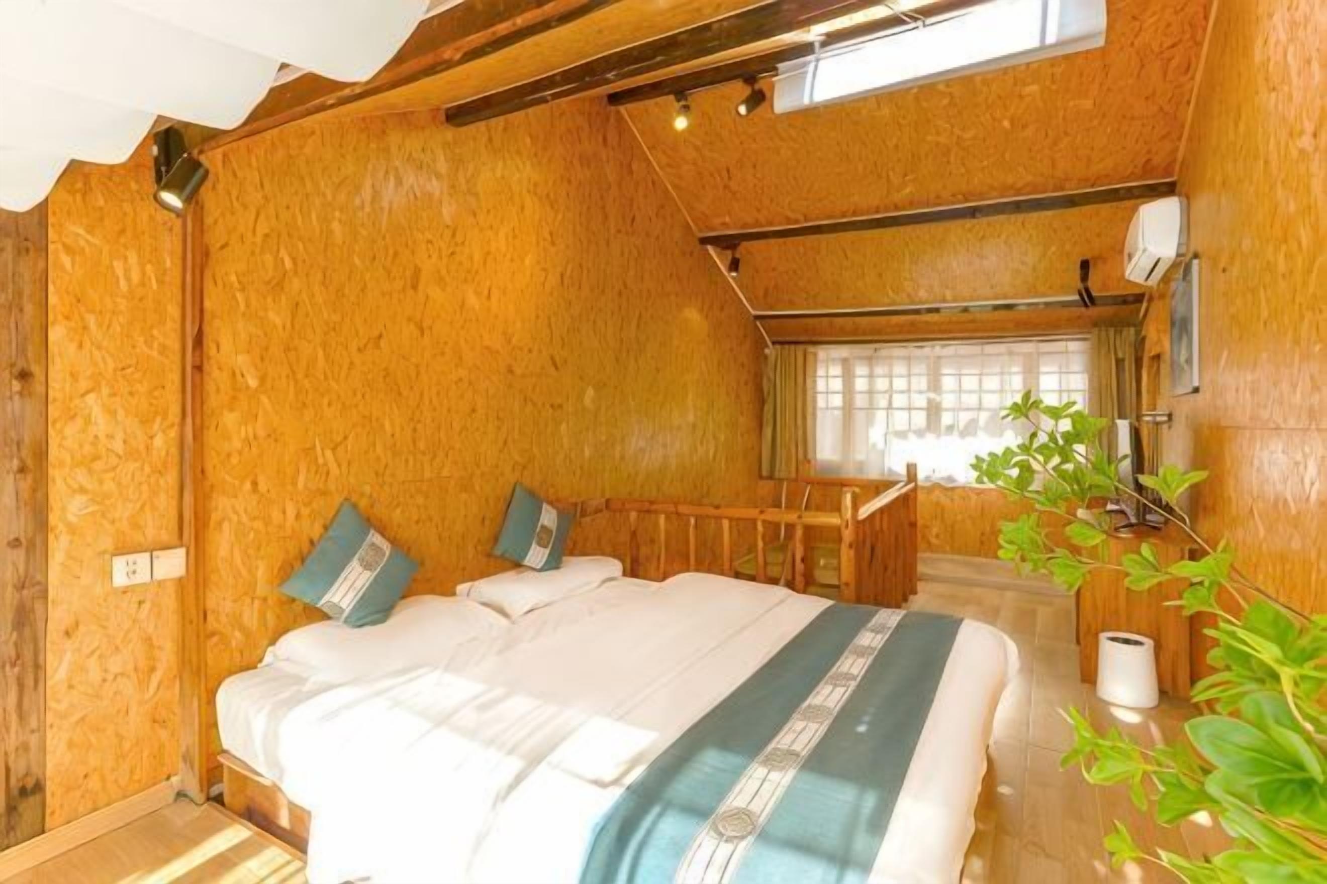 Ein Zimmer mit Holzboden, einem Bett, einem Fenster und einer Pflanze.