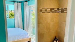 A bedroom with a bed, a wooden side table with toiletries, and a shower area with a towel rack. - South Park Hideaway (San Diego)
