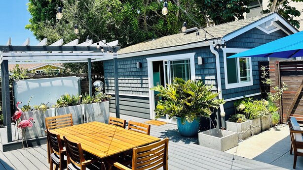 A wooden deck with a table and chairs, surrounded by potted plants and a blue awning. - South Park Hideaway (San Diego)