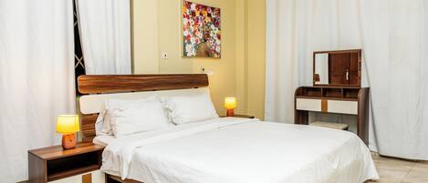 A hotel room with a wooden bed, white bedding, two bedside lamps, a nightstand, a mirror, and a wall-mounted air conditioner.