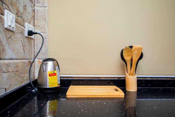 A kitchen counter with a kettle, a wooden cutting board, and a wooden utensil holder. - Maat Luxury Homes  (Santeo)