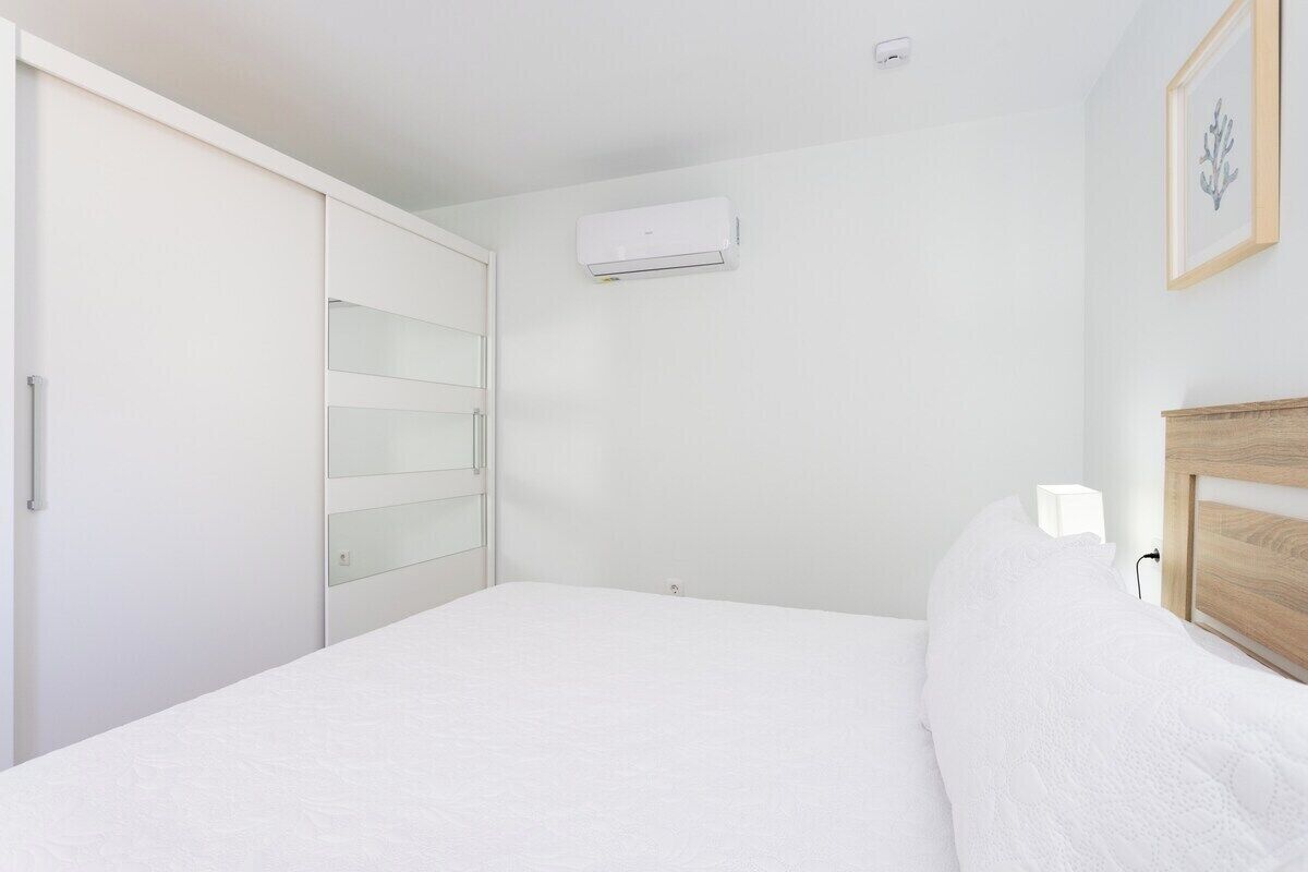 Un dormitorio con cama, armario, mesita de noche y aire acondicionado.