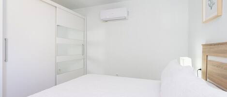 Un dormitorio con cama, armario, mesita de noche y aire acondicionado.