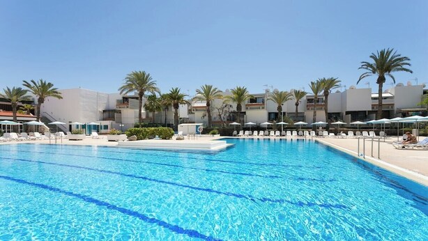 A large swimming pool with clear blue water, surrounded by lounge chairs and umbrellas, with palm trees and modern buildings in the background. - Home2Book Cozy Pool & Terrace Apartment, Arona (Arona)