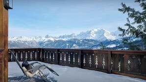Eine Holzdielen-Terrasse mit einem Metallstuhl, verschneitem Boden und Blick auf schneebedeckte Berge.