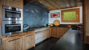 Eine moderne Küche mit Holzschränken, Edelstahlgeräten und einem großen Fenster mit Blick auf Grünflächen.