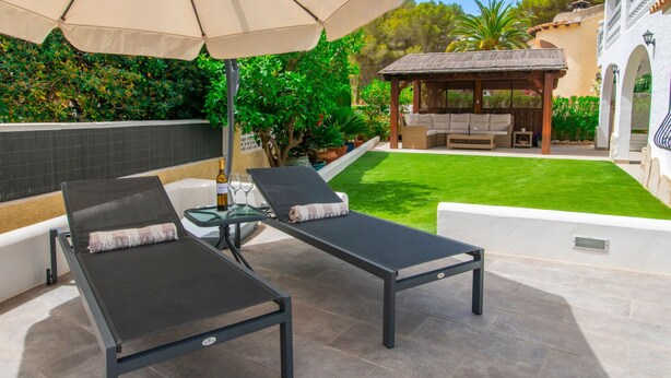 Two black lounge chairs with cushions, a glass table with a bottle and glasses, and a pergola with a barbecue. - Villa Kernow - comfortable 3 bedroom villa (Moraira)
