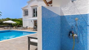 A poolside area with a blue-tiled shower enclosure, lounge chairs, and a white building with a balcony. - Villa Kernow - comfortable 3 bedroom villa (Moraira)