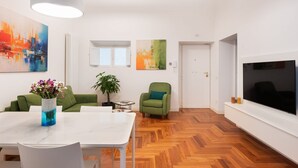 A modern living room with a white sofa, a green armchair, a dining table with chairs, and a large TV on the wall. - Idyllia | Vatican Stylish Flat (Roma)