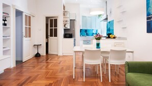 A modern kitchen with white cabinetry, a dining area with white chairs, and a wooden floor. - Idyllia | Vatican Stylish Flat (Roma)
