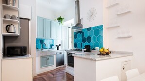 A modern kitchen with white cabinets, a blue hexagonal backsplash, and a central island with a fruit bowl. - Idyllia | Vatican Stylish Flat (Roma)
