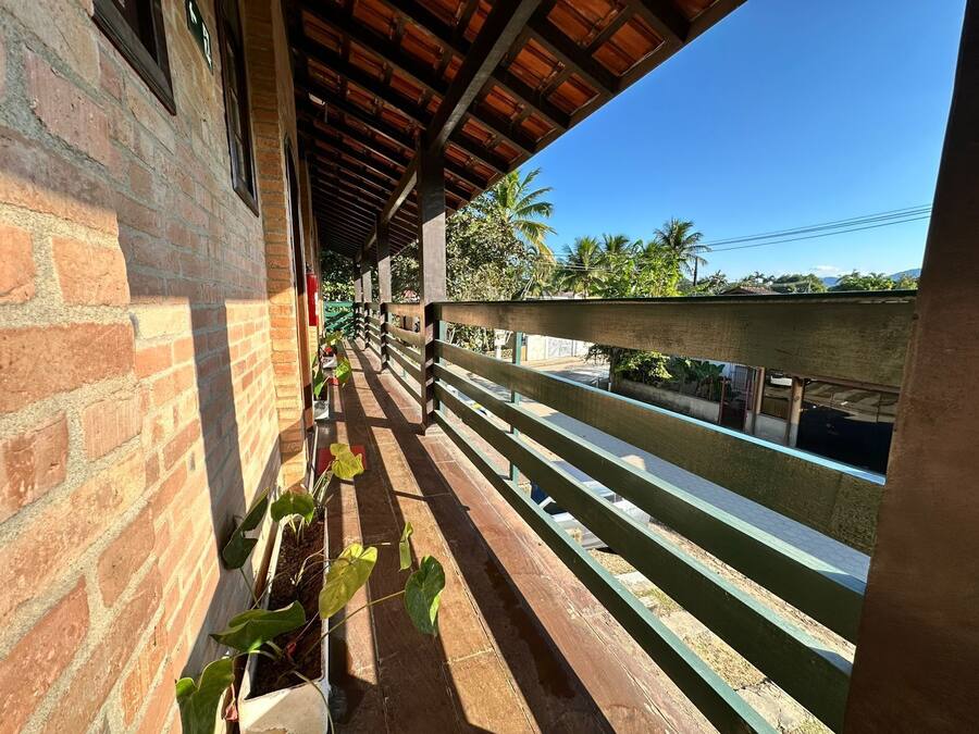 A covered balcony with a brick wall, wooden railing, and potted plants.