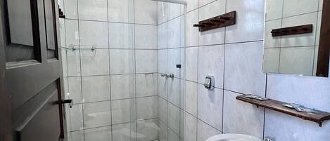 Casa de banho com chuveiro, sanita, lavatório e espelho.