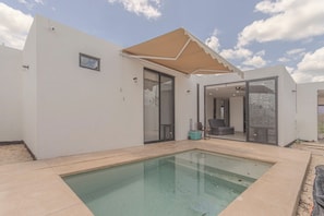 A modern house with a swimming pool, a covered patio, and a glass door leading to an indoor living area.