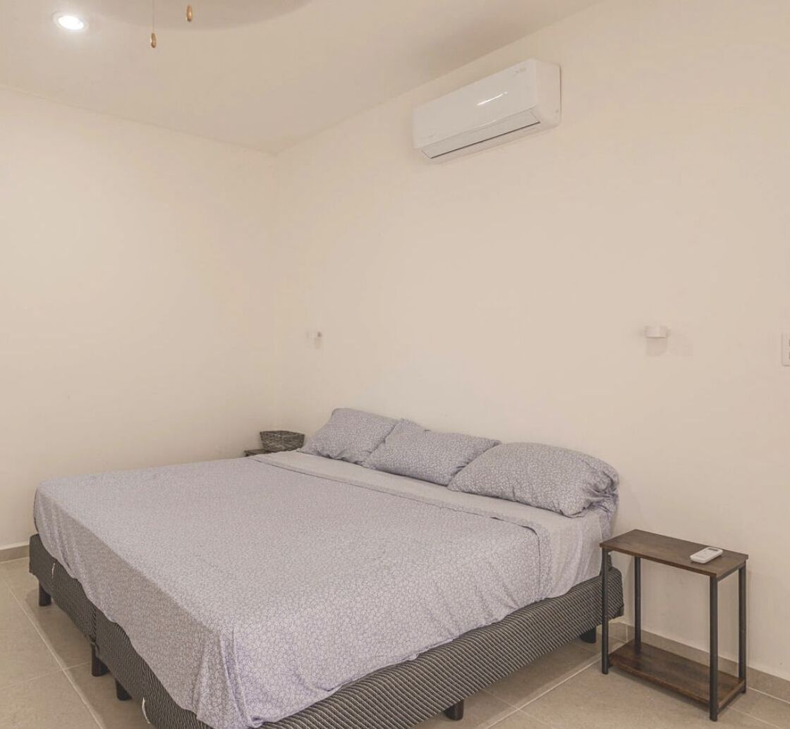 A bedroom with a bed, a bedside table, and an air conditioning unit on the wall.
