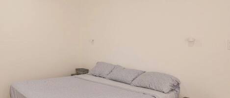 A bedroom with a bed, a bedside table, and an air conditioning unit on the wall.