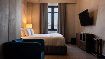 Habitación de hotel con cama, escritorio, silla, televisión y ventana con cortinas.