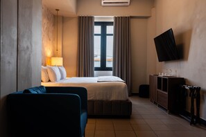 A hotel room with a bed, a desk, a chair, a TV, and a window with curtains. - The Oliver Hotel - Adults Only (San Juan)