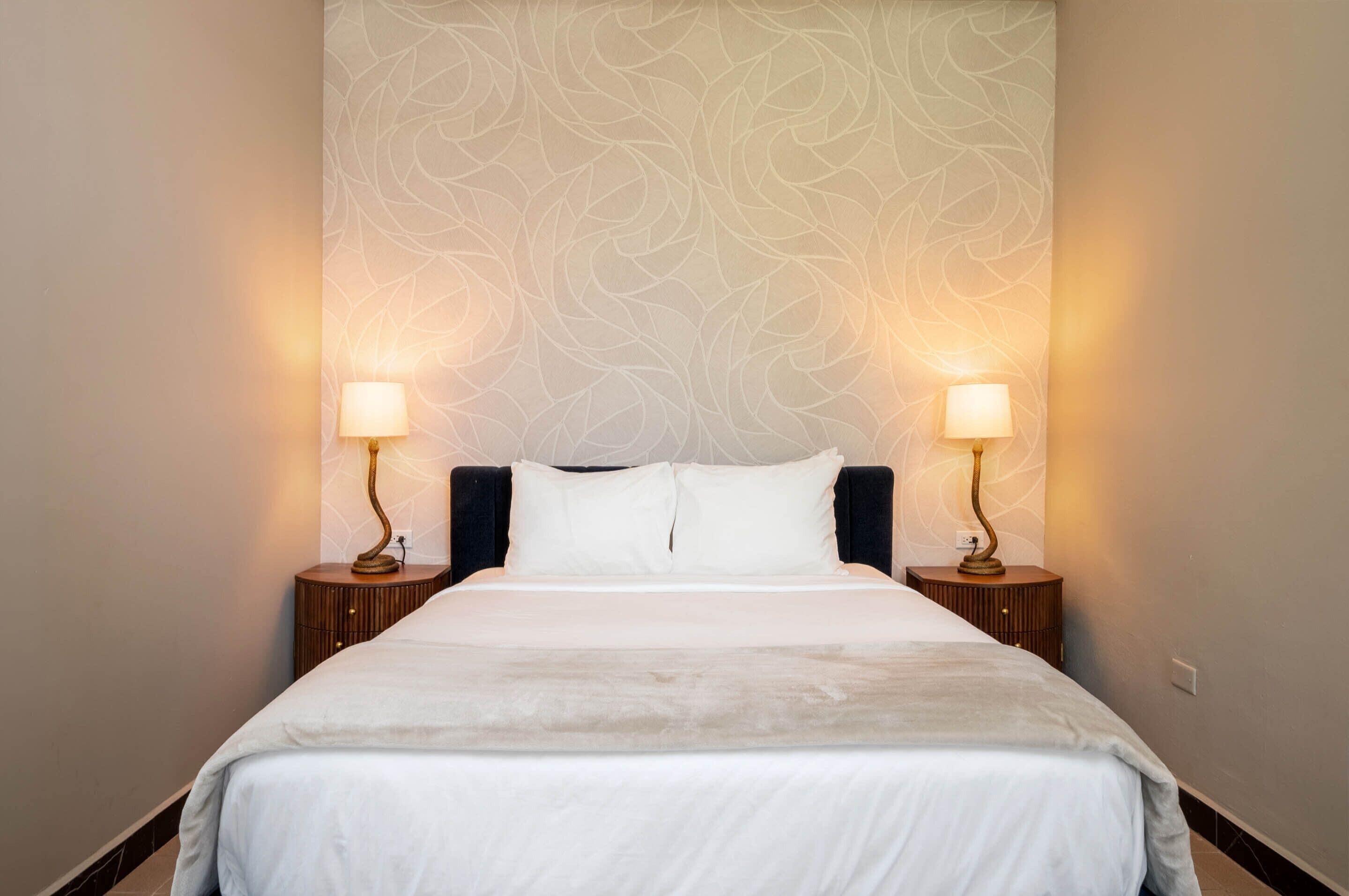 A hotel room with a large bed, two bedside lamps, and a patterned wallpaper.