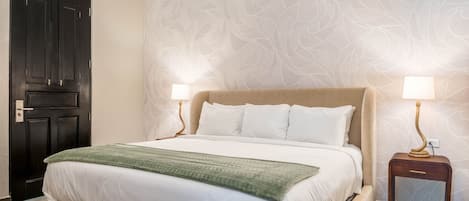 A hotel room with a bed, two bedside lamps, a nightstand, and a patterned wallpaper.