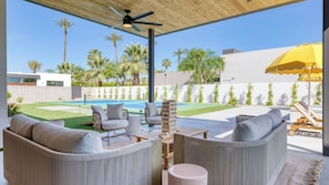 A covered outdoor seating area with a pool, lounge chairs, and a wooden table.