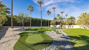 Ein gepflegter Golfplatz mit Putting-Green, Sandbunkern und verschiedenen Bäumen.