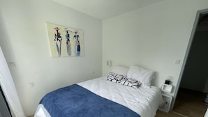 A bedroom with a bed, white walls, a painting, and a nightstand with a lamp. - Pornichet - Apartment near Hippodrome (PORNICHET)