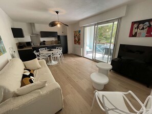 Un salon moderne avec un canapé blanc, un canapé noir, une table à manger avec des chaises, un ventilateur de plafond et une grande fenêtre donnant sur l’extérieur.
