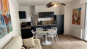 A modern living room with a sofa, a dining table with chairs, a kitchen area with a microwave, a kettle, and a refrigerator. - Pornichet - Apartment near Hippodrome (PORNICHET)