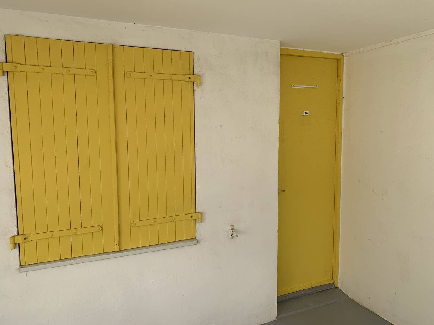 A room with a yellow door and a yellow window shutter.