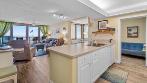 Een ruime woonkamer met een keukeneiland, een eettafel en een bank.