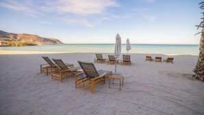 A beach with wooden lounge chairs and umbrellas, a clear sky, and a calm sea.