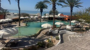 A pool area with lounge chairs and umbrellas, surrounded by palm trees, with a view of the sea.