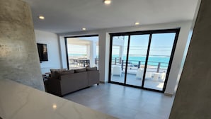 A spacious living area with a large sliding glass door leading to a balcony with a view of the ocean.
