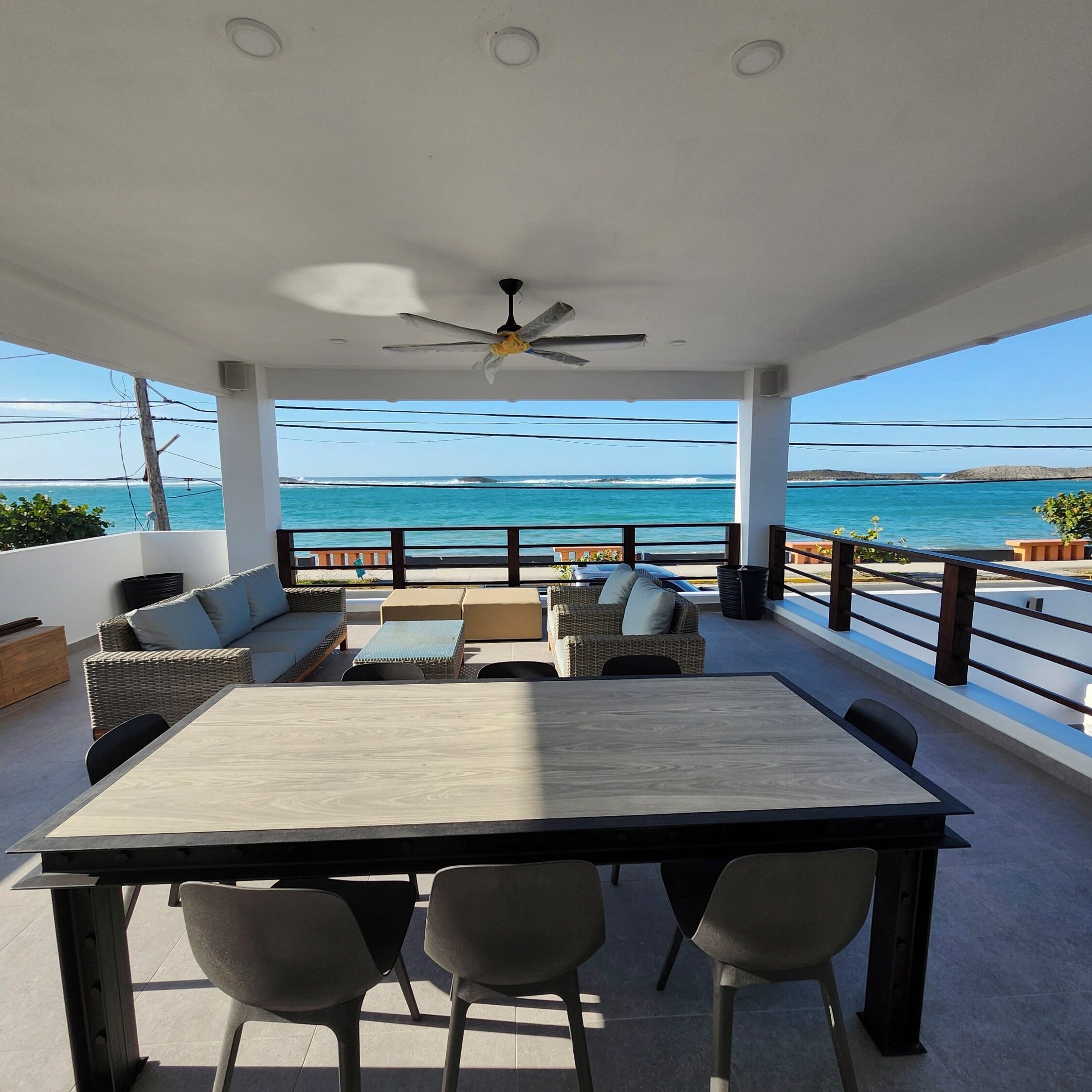 A covered outdoor seating area with a view of the ocean, a table, and chairs.