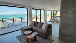 A modern living room with a large sofa, two round wooden side tables, and a view of the ocean through large windows.