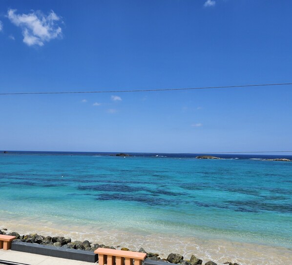 Ein Strand mit klarem türkisblauem Wasser, einer felsigen Küstenlinie und einer entfernten Insel.