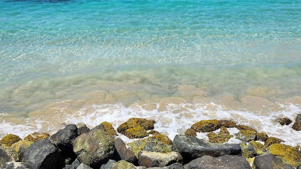 A coastal scene with clear turquoise waters, rocky shoreline, and distant islands.
