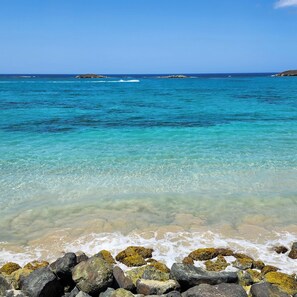 Paisaje costero con aguas turquesas cristalinas, costa rocosa y islas distantes.